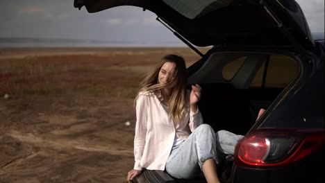 Portrait-of-a-woman-traveler-having-a-break-sitting-in-car-trunk-barefoot,-relaxing