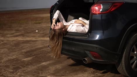Portrait-of-a-long-haired-woman-traveler-having-a-break-laying-in-car-trunk-and-relaxing