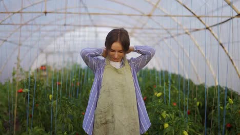 Young-woman-gardener-putting-on-apron,-ready-for-work-at-plant-shop-greenhouse