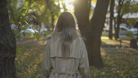 Rear-view-of-and-elegant-woman-walking-by-autumn-park-in-trench-coat