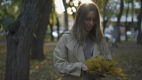 Thoughtful-woman-with-pile-of-golden-leaves-in-hands-in-sunny-autumn-park