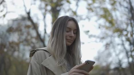 Woman-reading-messages-or-surfing-internet-from-phone-at-autumn-park,-overview-footage