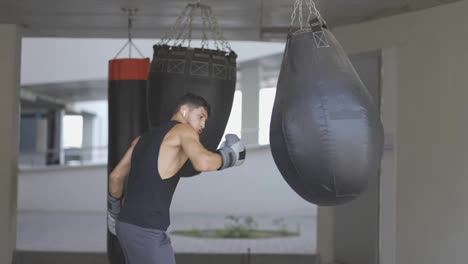 The-man-executes-strong-blows-in-the-boxing-bag,-outdoors