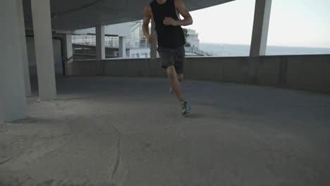 Unrecognizable-athlete-runs-around-by-levels-of-and-empty-parking-garage,-front-view