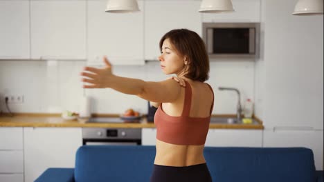 Mujer-Gira-Sus-Brazos,-Practicando-Yoga-En-Casa,-Vista-Trasera