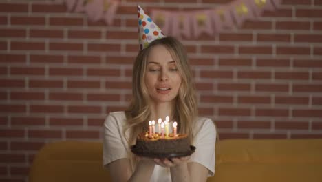 Portrait-of-pretty-girl-holding-birthday-cake-and-blowing-candles-at-party
