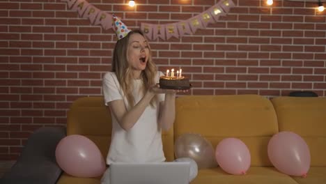 Excited-girl-celebrates-birthday-online-by-webcam-holding-cake-with-candles
