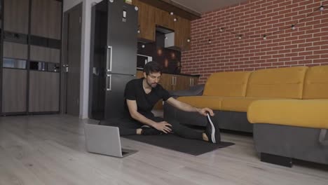 Guy-watching-flexibility-online-training-on-laptop-sitting-on-yoga-mat