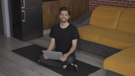 Portrait-of-a-man-sitting-on-the-mat-on-the-floor-with-laptop-at-home