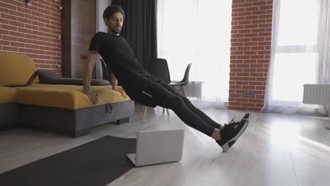 Man-athletic-doing-push-up-leaning-on-sofa-at-home-with-laptop