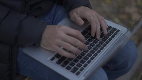Unrecognizable-man-sitting-on-the-bench-in-the-park,-typing-on-the-laptop