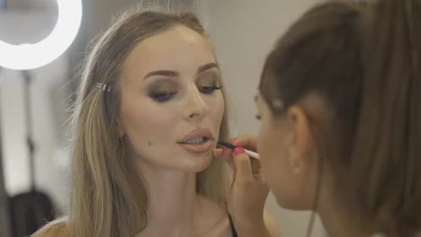 The-make-up-artist-applying-nude-lipstick-to-the-model's-lips-in-studio