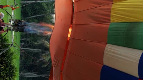 Vertical-slow-motion-close-up-shot-of-a-colorful-and-large-hot-air-balloon-inflated-with-a-burner-with-gas-and-flames-for-a-balloon-flight-in-bali-indonesia-in-ubud