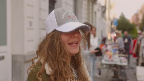 Fröhliche-Junge-Frau-Mit-Weißer-Und-Grauer-Roland-Garros-Mütze,-Lächelt-Und-Winkt-In-Die-Kamera