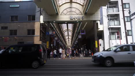 Menschen-Warten-An-Der-Kreuzung,-Während-Der-Verkehr-Vor-Der-Tanukikoji-Einkaufspassage-In-Sapporo-Vorbeifährt