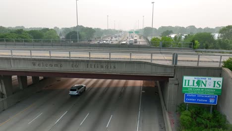 Welcome-to-Illinois-sign-and-text-on-bridge-above-interstate-highway-headed-towards-Chicago,-IL