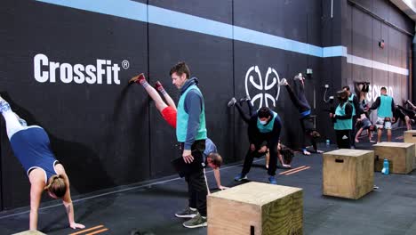 People-doing-a-crossfit-challenge-with-a-coach-competing-to-each-other-while-doing-exercises-in-open-gym