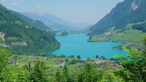 Beautiful-blue-lake-in-Switzerland,-surrounded-by-mountains-and-green-grass,-on-a-clear-sunny-day