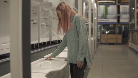 Blonde-woman-is-choosing-a-new-ceramic-sink-in-a-store