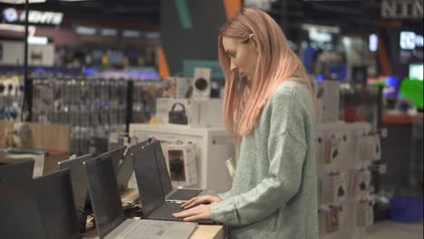 Woman-chooses-a-laptop-in-a-device-store,-carefully-selecting