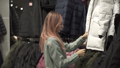 Woman-is-taking-a-new-down-jacket-from-a-rack-to-fit-it