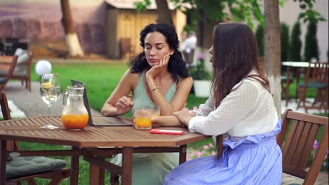 Two-women-sitting-at-the-outdoors-cafe---talking,-sharing-news,-brunette-girl-listen-carefully