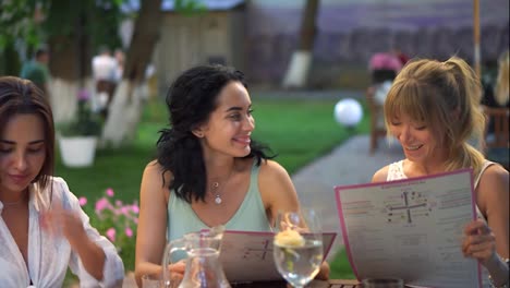 Portrait-of-three-pretty-girlfriends-reading-menu-and-having-fun-together-in-the-cafe-outdoors-in-the-public-park
