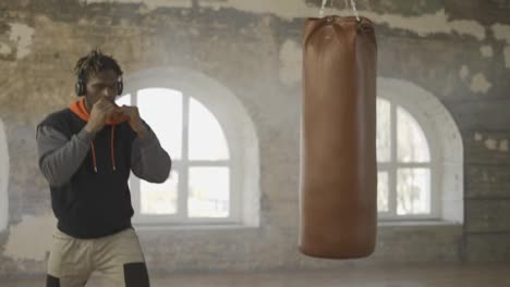 Afroamerikanischer-Junger-Männlicher-Boxer,-Der-In-Der-Hellen-Halle-Schattenboxen-Mit-Kopfhörern-übt