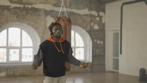 Male-boxer-skipping-the-rope-in-and-empty-hall,-listen-music-in-headphones