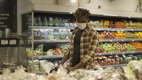 Man-in-mask-push-cart,-choosing-fruits-and-vegetables-in-the-fresh-produce-section
