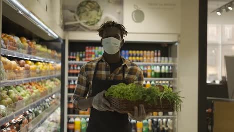 Male-worker-in-mask-at-the-store-walks-with-basket-full-of-greens