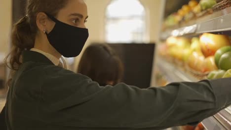 Two-women-choosing-bio-fruits-in-supermarket-together,-wearing-mask