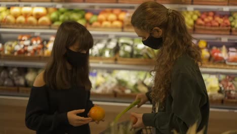 Two-women-in-masks-choosing-bio-fruits-in-supermarket-together