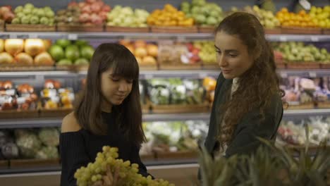 Zwei-Fröhliche-Frauen-Wählen-Gemeinsam-Bio-Früchte-Aus---Trauben-Im-Supermarkt