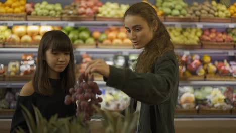 Two-cheerful-girls-choosing-bio-fruits---grape-in-supermarket-together