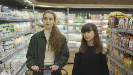 Teen-girl-and-her-mom-or-sister-shopping-in-the-supermarket-with-cart