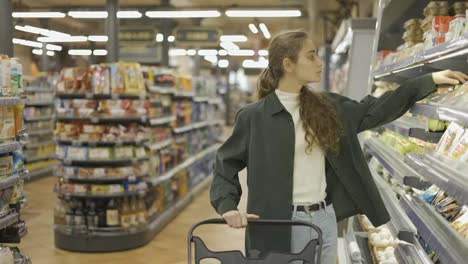 A-woman-in-a-supermarket-pushing-trolley,-choosing-cheese-in-milk-section