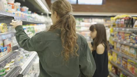 Teen-girl-and-her-mom-or-sister-shopping-in-the-supermarket-with-cart,-rear-view