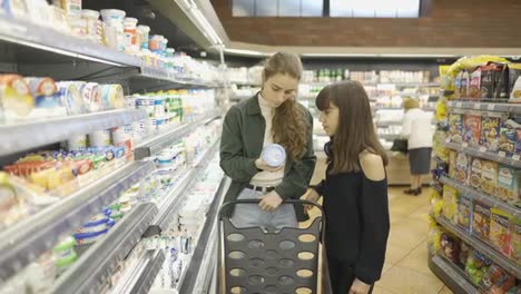 Teen-girl-and-her-mom-or-sister-shopping-in-the-supermarket-with-cart,-slow-motion