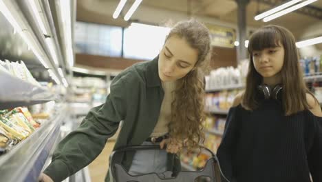 Teen-girl-and-her-mom-or-sister-shopping-in-the-supermarket,-read-the-labels