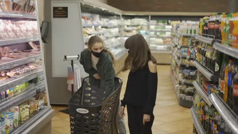 Teen-girl-and-her-mom-or-sister-shopping-in-the-supermarket-with-cart,-wearing-masks