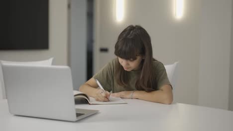 Brunette-teen-girl-sitting-at-the-desk-doing-her-homework-using-a-laptop