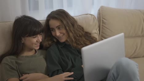 Two-pretty-caucasian-girls-having-fun-while-watching-comedy-movie-on-laptop-on-couch-in-room