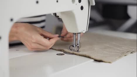 Closeup-of-a-young-woman's-hands-sewing-beige-fabric-with-a-sewing-machine