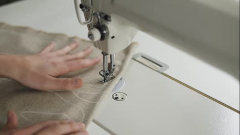 Closeup-of-a-young-woman's-hands-sewing-beige-fabric-with-a-design