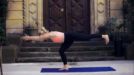 Mujer-Haciendo-Yoga-Sobre-Un-Porche-Con-Una-Gran-Puerta-De-Madera,-Vista-Frontal