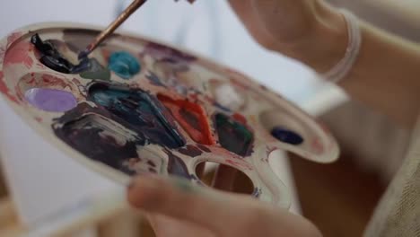 Female-artist-mixes-paints-on-a-palette-draws-woman-body-on-a-canvas