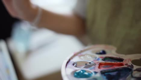 Close-up-woman-artist-painting-picture-on-canvas-in-art-studio-using-palette