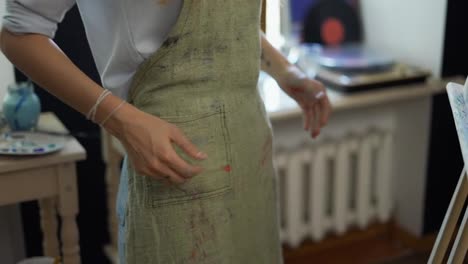 Female-artist-in-dirty-apron-wipes-her-hands-in-art-studio-close-view