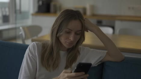 Calm-woman-surfing-in-Internet-at-phone-in-apartment-on-couch